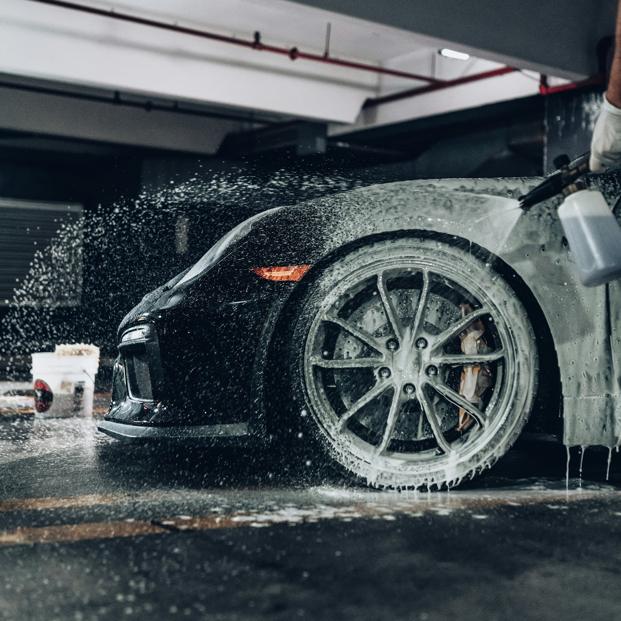 Snow foam being sprayed over a black sports car and its alloy wheel