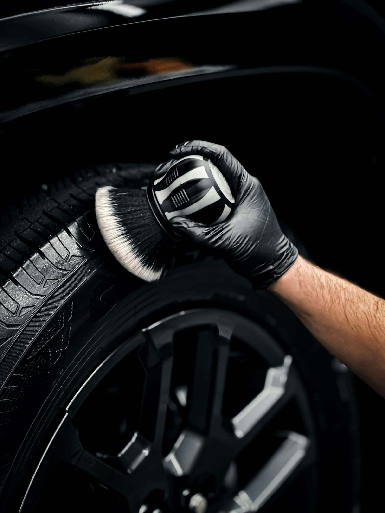Gloved hand scrubbing a tire sidewall with a detailing brush